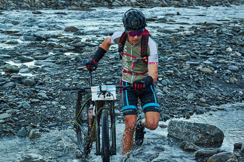 Rider carrying a bike across a braided river